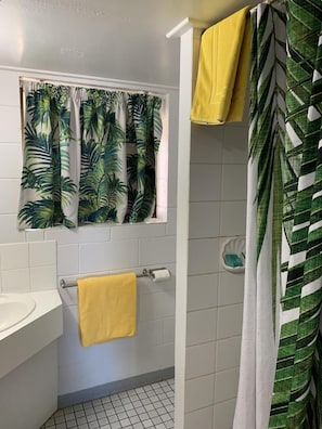 A bathroom with a shower curtain featuring a leaf pattern, a yellow towel hanging on a rack, and a white sink.