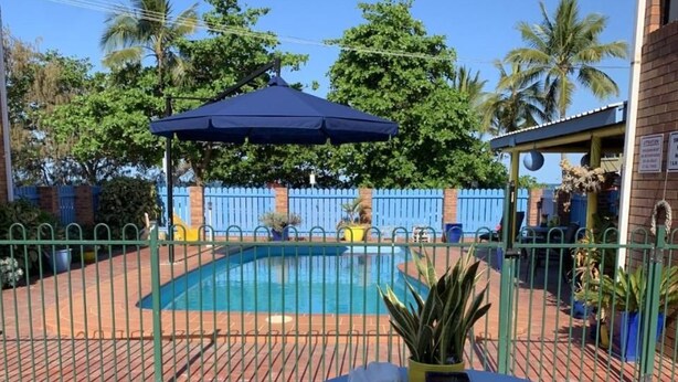Zona de piscina exterior con mesa y sillas, rodeada por una valla y plantas en macetas.
