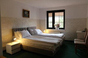 A bedroom with two beds, a nightstand, a chair, a window with a view, and a radiator.