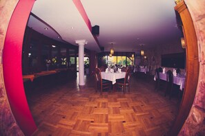A dining area with wooden parquet flooring, white tables, and chairs.