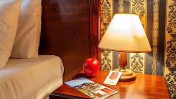 A hotel room with a bed, a nightstand with a lamp, an apple, and a brochure.