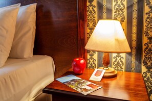 A hotel room with a bed, a nightstand with a lamp, an apple, and a brochure.