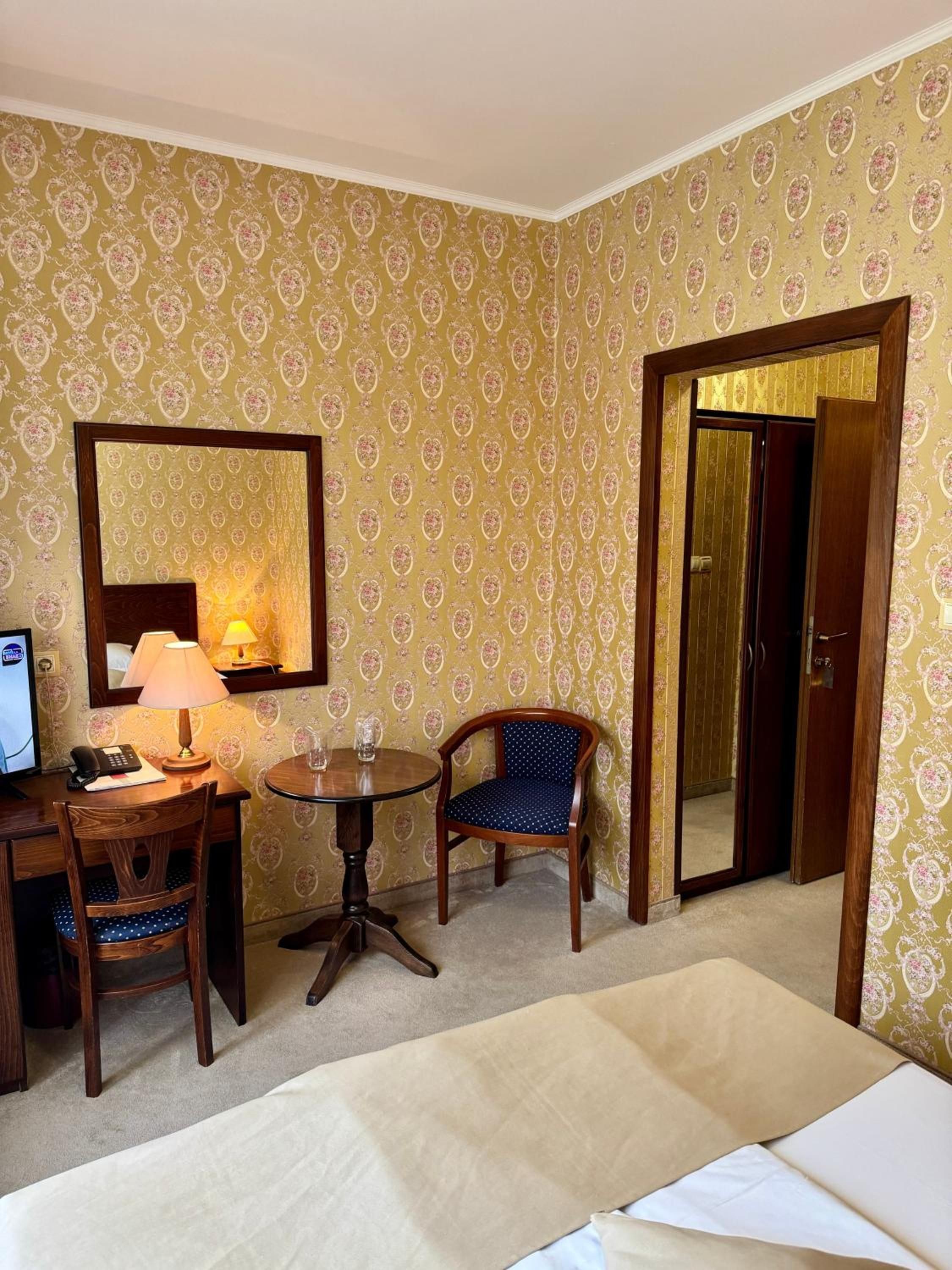 A hotel room with a bed, a desk with a lamp, a chair, and a mirror.