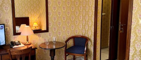 Una habitación de hotel con una cama, un escritorio con lámpara, una silla y un espejo.