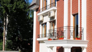 A two-story building with a brick facade, white trim, and a balcony with potted plants.