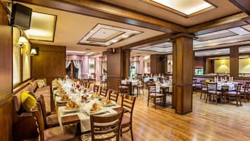 A spacious dining area with multiple tables set for service, wooden flooring, and a high ceiling with recessed lighting.