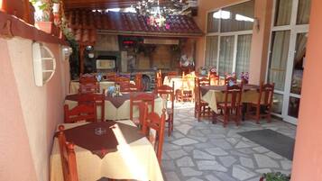 Un área de comedor al aire libre con varias mesas y sillas, piso de piedra y techo de madera.