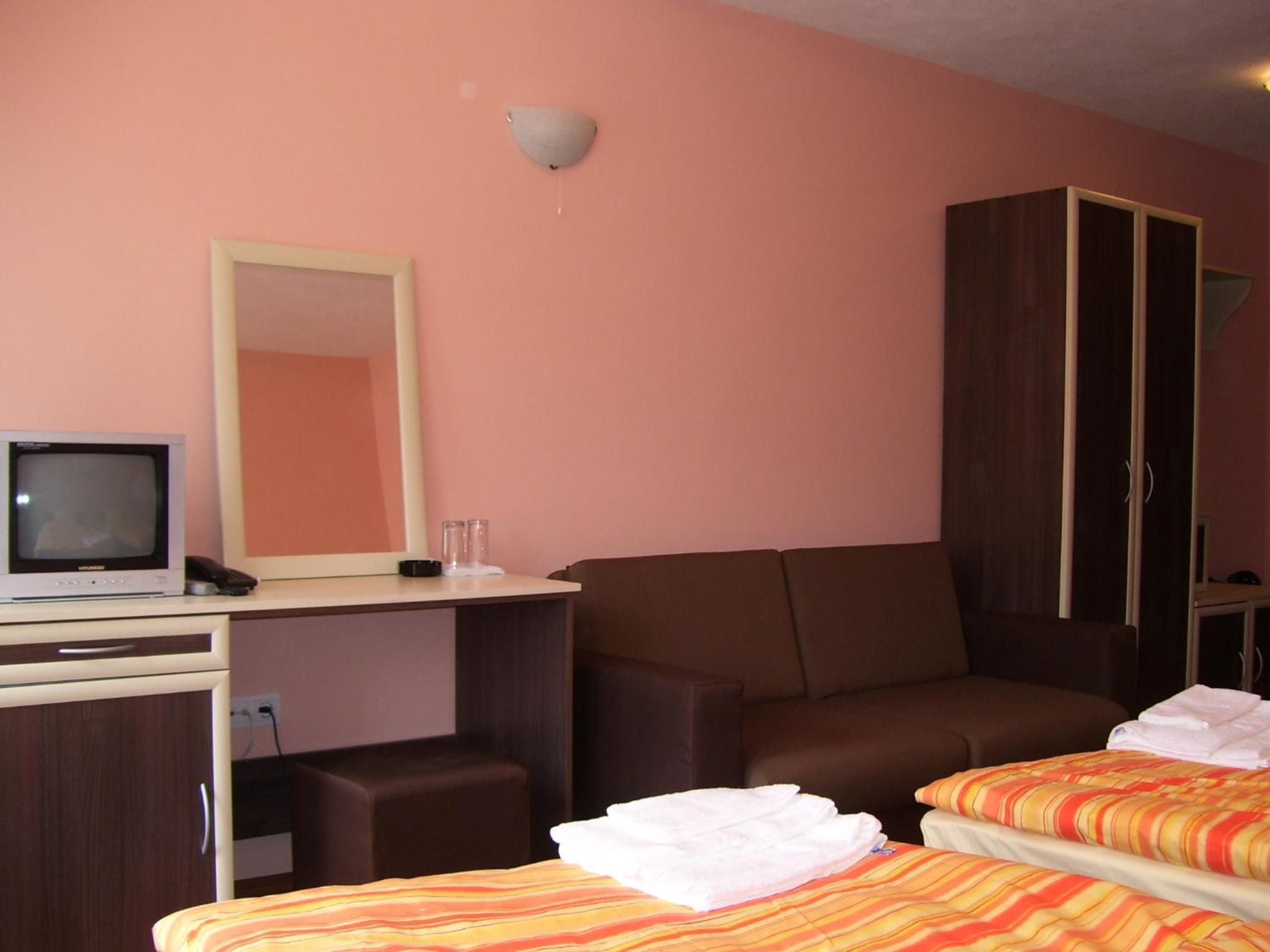 Quarto de hotel com uma cama, uma escrivaninha com televisão, um espelho e um guarda-roupa.