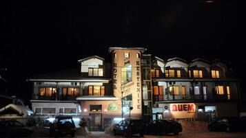 Un hotel de varios pisos, con un letrero de restaurante a la vista y varios coches estacionados frente a él.