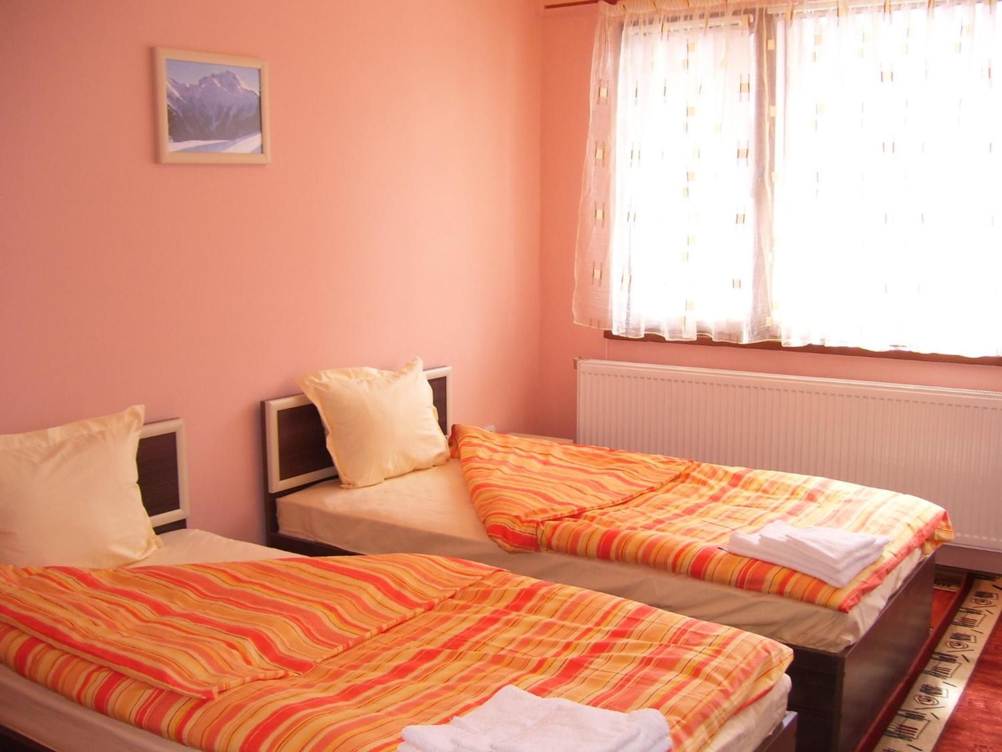 A room with two beds, a window with curtains, and a picture on the wall.