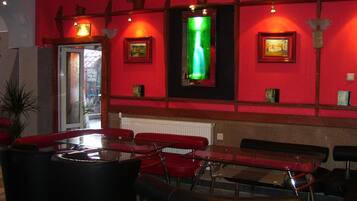 Una habitación con paredes rojas, un panel de vidrio, sillas rojas, una mesa y una pantalla iluminada en verde.