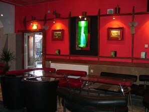 A red-walled room with a glass partition, red chairs, a table, and a green-lit display. - Kestenite Family Hotel (Samokov)