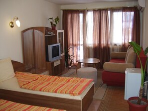 A hotel room with a bed, a TV, a desk, a chair, a sofa, and a potted plant. - Kestenite Family Hotel (Samokov)