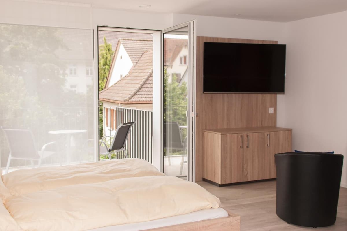 A bedroom with a bed, a TV mounted on the wall, and a sliding glass door leading to an outdoor area.