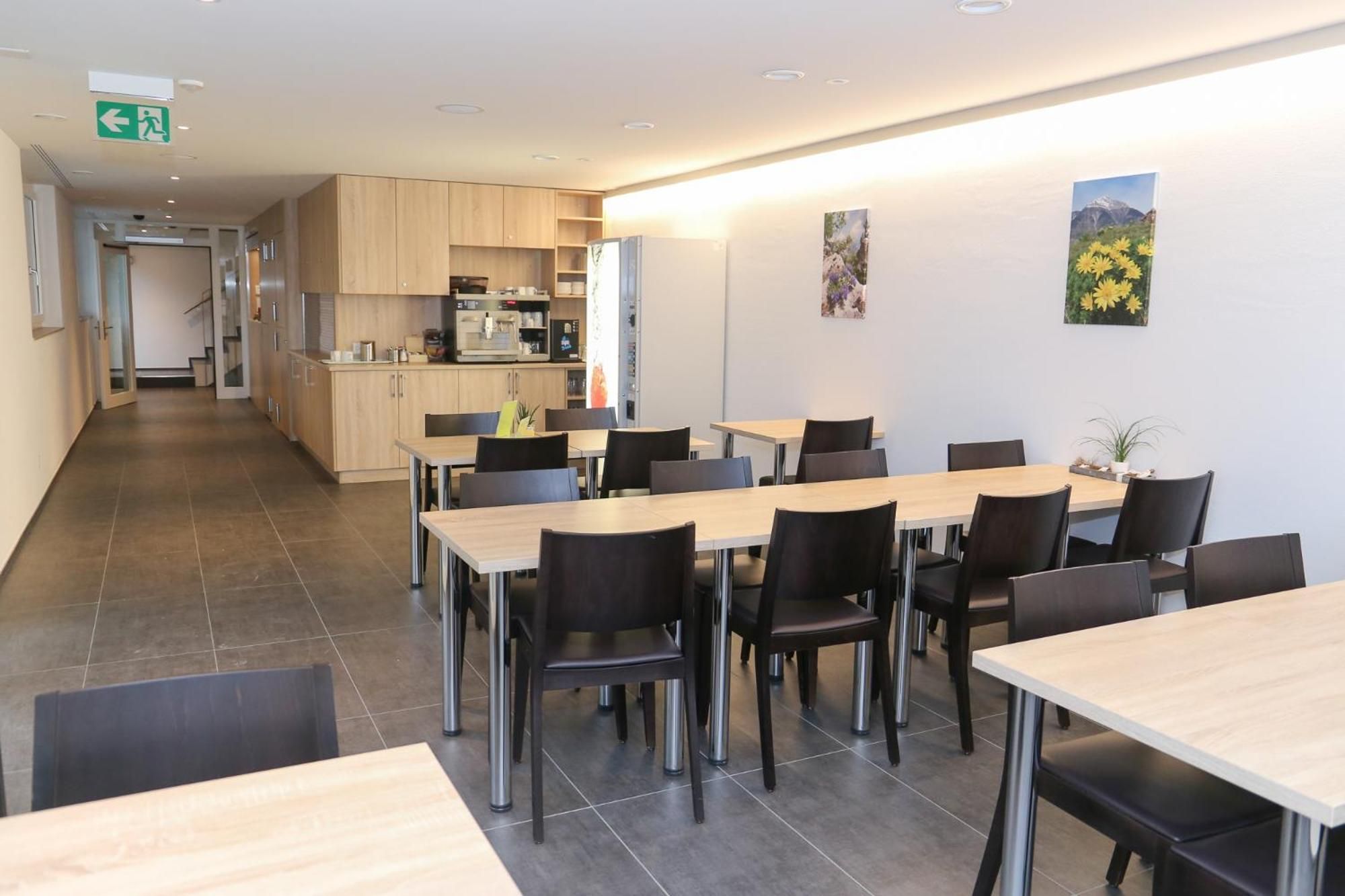 A modern dining area with multiple tables and chairs, a kitchen in the background, and artwork on the walls.