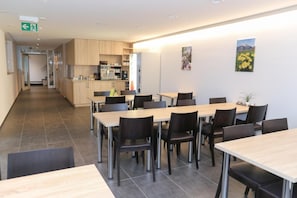 A modern dining area with multiple tables and chairs, a kitchen in the background, and artwork on the walls. - Hotel Traube Garni (Küttigen)