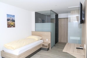 A modern bedroom with a bed, a small bedside table, a TV, and a glass partition. - Hotel Traube Garni (Küttigen)