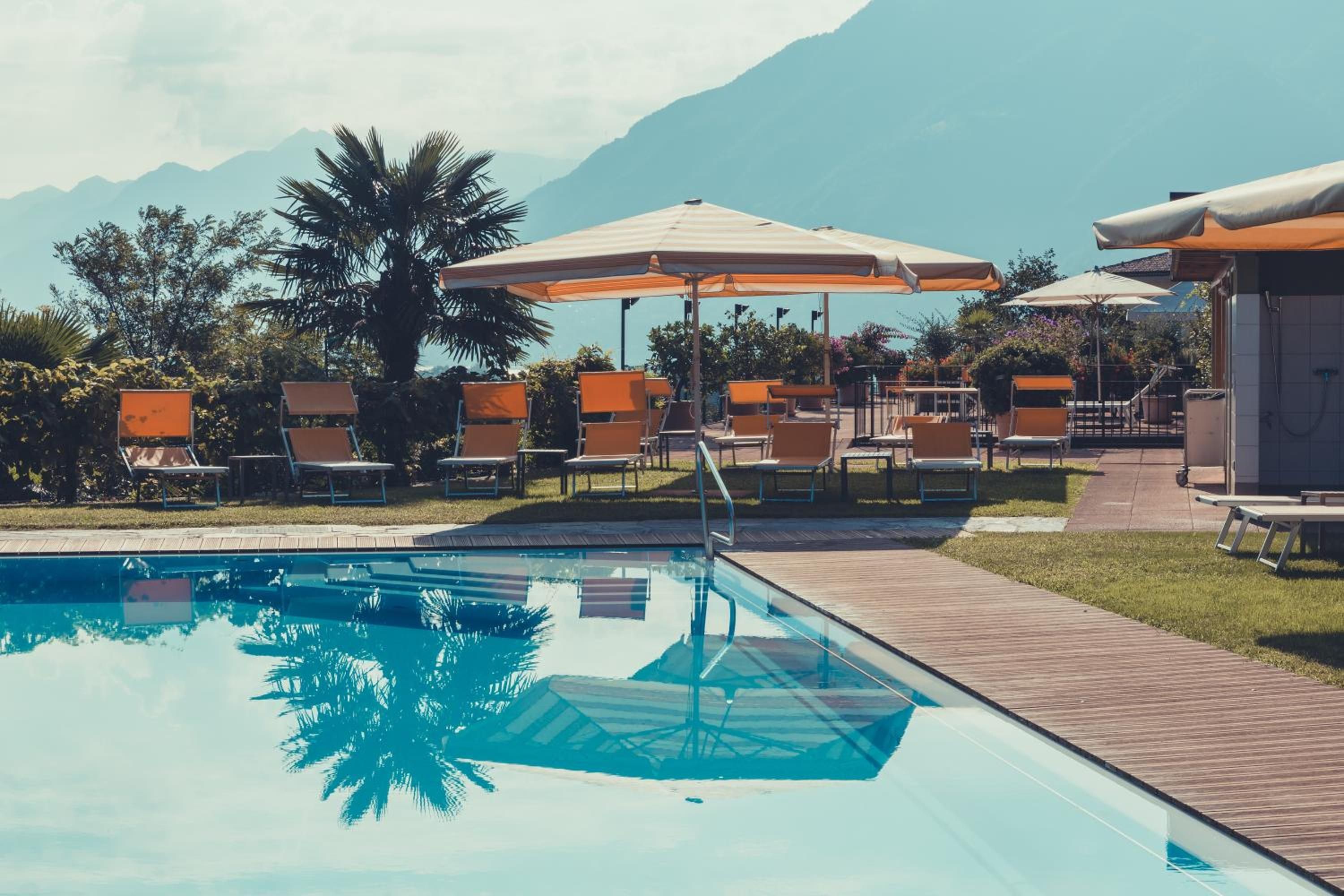 A swimming pool with lounge chairs and umbrellas, surrounded by greenery and mountains.