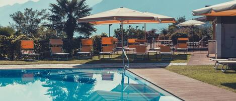 A swimming pool with lounge chairs and umbrellas, surrounded by greenery and mountains.