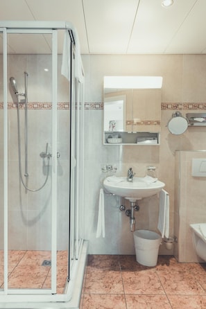 A modern bathroom with a glass-enclosed shower, a sink with a mirror above it, and a toilet. - Hotel Tobler (Ascona)