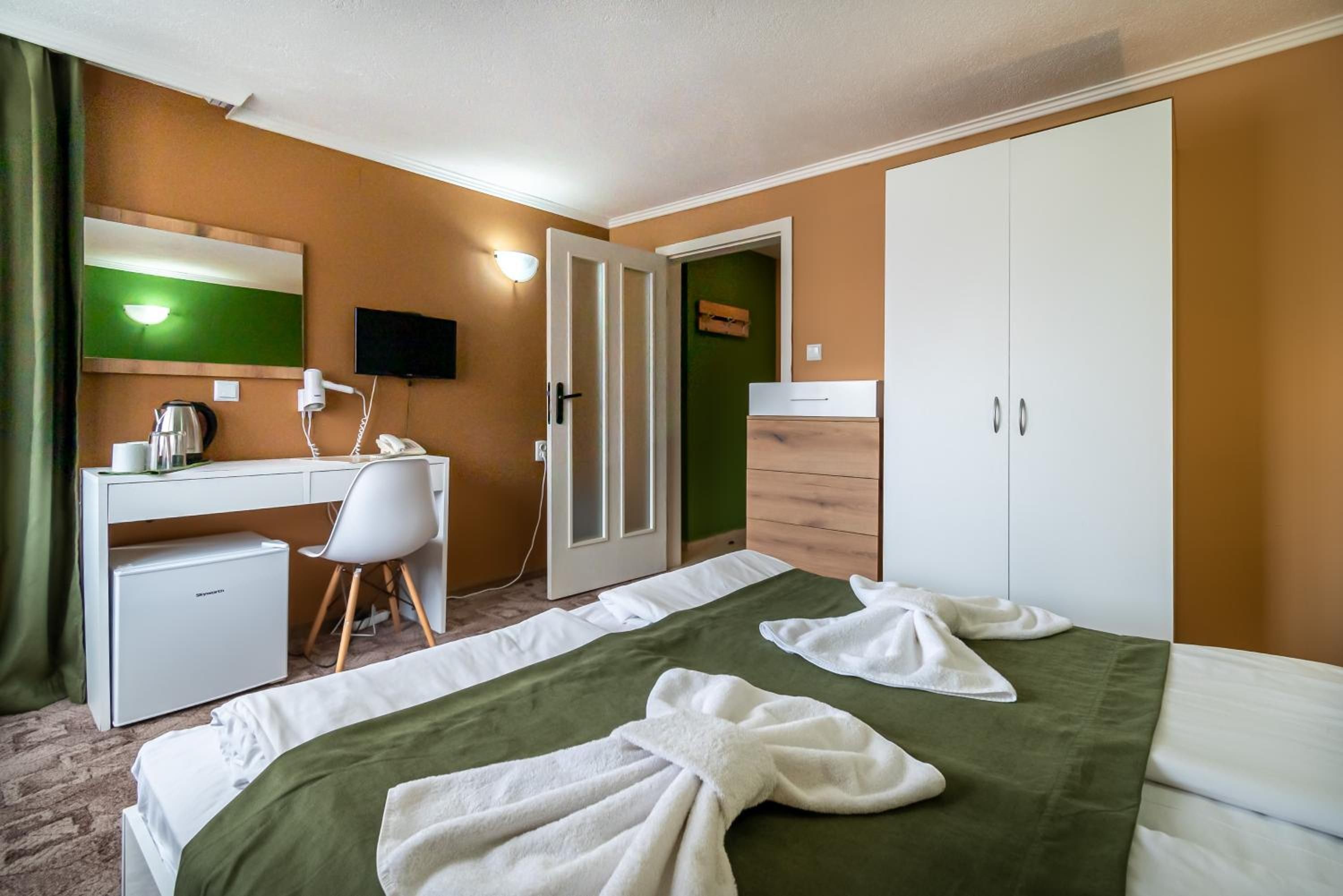 A hotel room with a bed, a desk, a chair, a wardrobe, and a television.