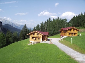Dos chalets de madera con techos rojos, un camino de grava y montañas al fondo.