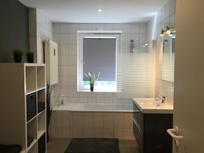 A modern bathroom with a window, a bathtub, and a vanity. - Engels Hof (Wolfsburg)