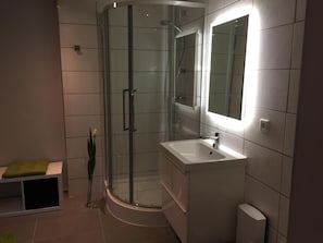 Un baño moderno con ducha envuelta en vidrio, lavamanos blanco y espejo.