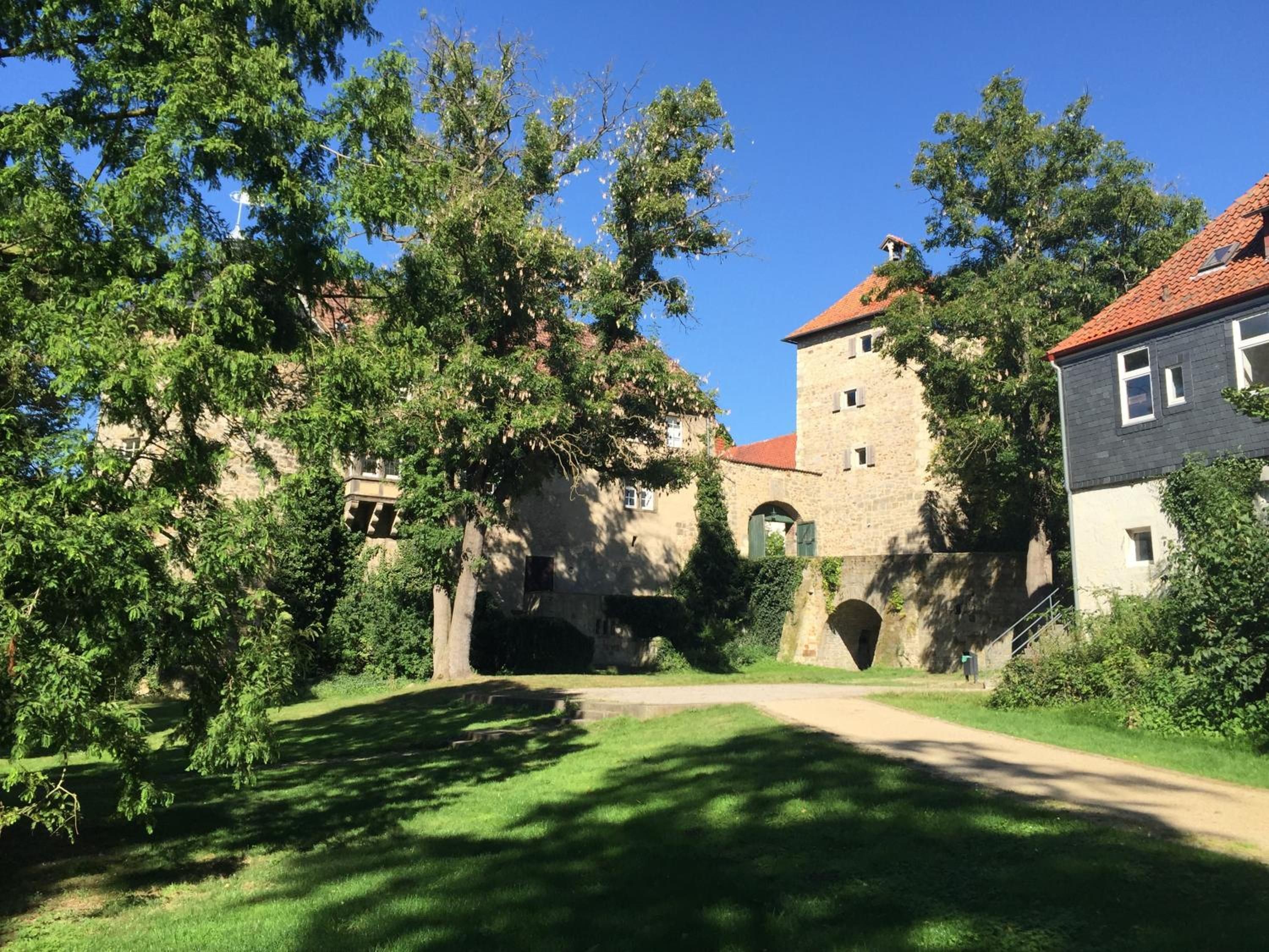 Un edificio histórico con una torre, rodeado de exuberante vegetación y un cielo despejado.