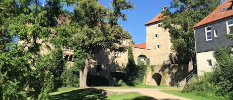 En historisk byggnad med ett torn, omgiven av frodig grönska och en klar himmel.