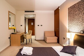 Quarto de hotel com cama, escrivaninha, cadeira, sofá, espelho e parede com estampa de leopardo.