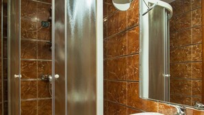 Un baño moderno con ducha de vidrio, lavamanos blanco y un espejo grande.