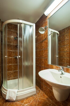 Un baño moderno con ducha de vidrio, lavamanos blanco y un espejo grande.