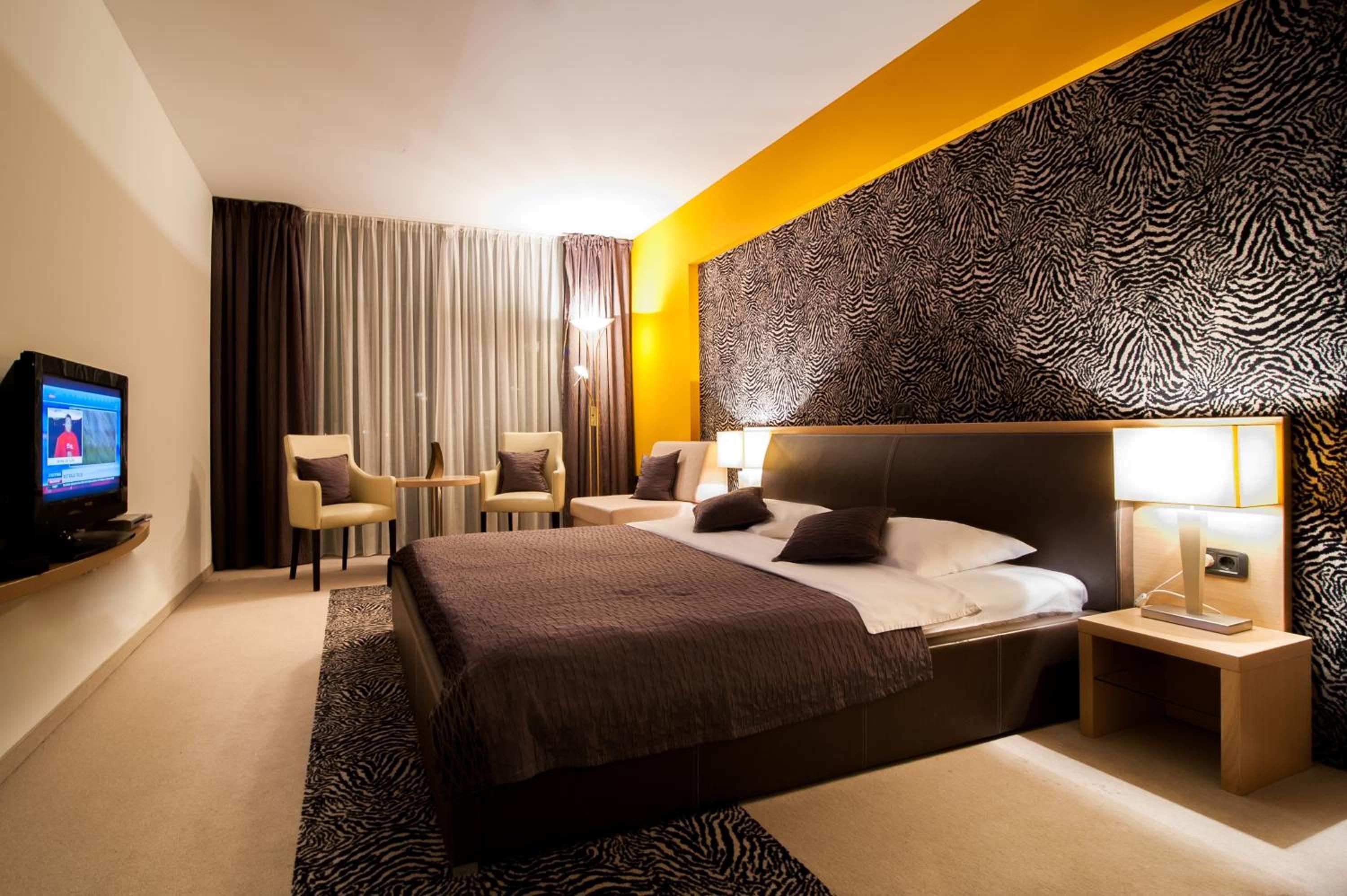 Ein Hotelzimmer mit einem Bett, einem Fernseher, zwei Stühlen, einer Lampe und einer Wand mit ZEBRA-Muster.