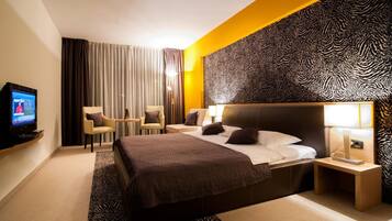 A hotel room with a bed, a television, two chairs, a lamp, and a zebra-patterned wall.