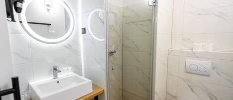 Een moderne badkamer met een wit wastafelmeubel, een spiegel met ronde verlichting, een douchecabine van glas en een toilet.