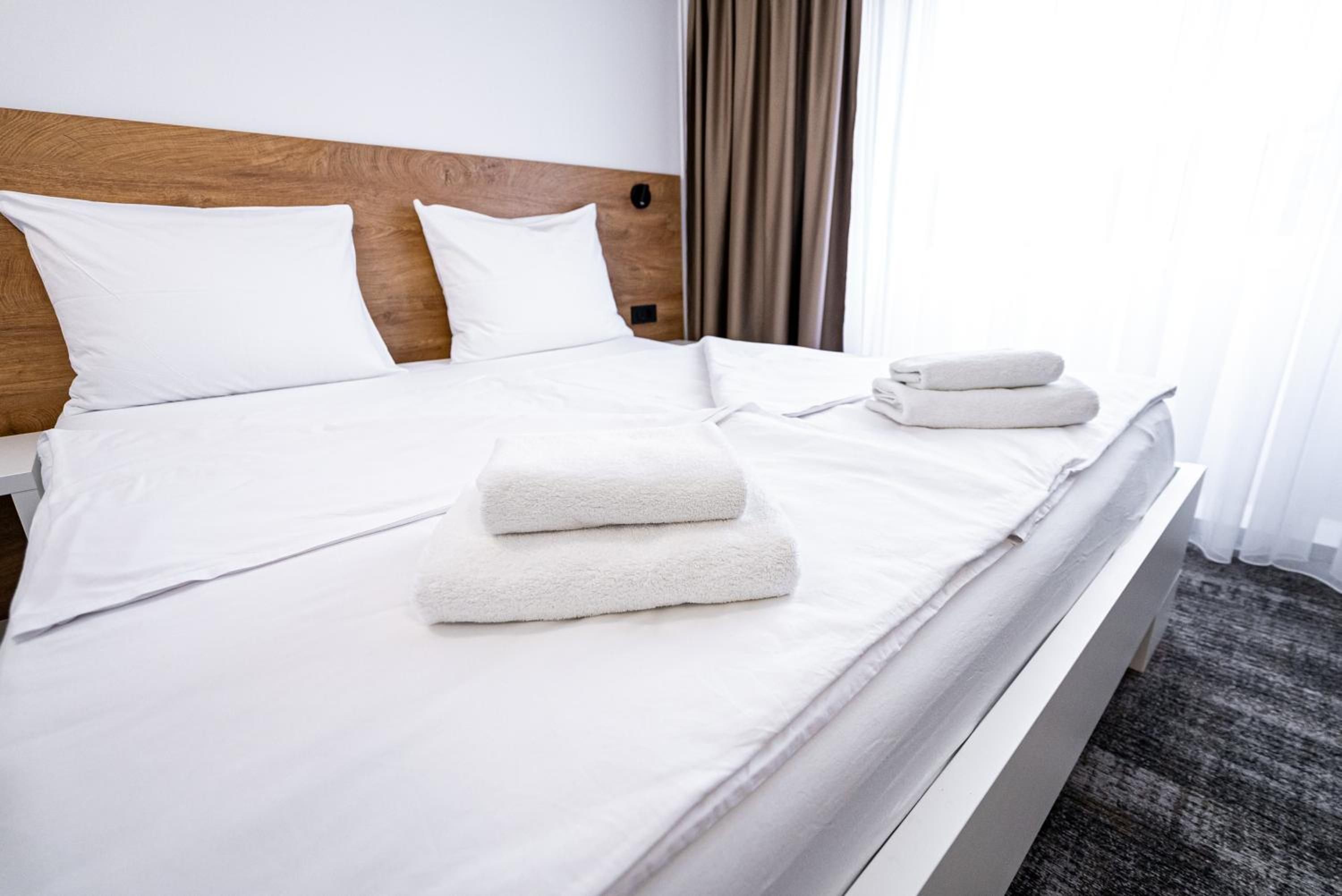 A neatly made bed with white linens, two folded towels, and a wooden headboard.