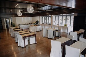Un amplio salón con varias mesas redondas, sillas blancas y una moderna lámpara de araña.