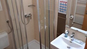 Un baño con ducha envuelta en vidrio, un lavabo blanco y un inodoro.