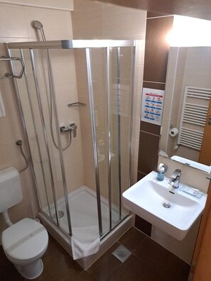 Casa de banho com chuveiro em cabine de vidro, lavatório branco e sanita.