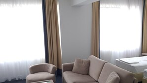 Una habitación de hotel con sofá, sillón, reposapiés y cama.