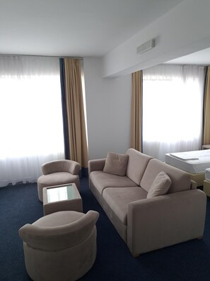 Quarto de hotel com sofá, poltrona, banquinho e uma cama.