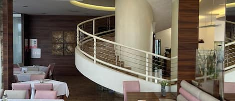 A modern restaurant with a curved seating area, a wooden floor, and a glass railing overlooking a lower level.