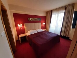 A hotel room with a large bed, two bedside tables, a red accent wall, and a painting above the bed.
