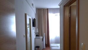 Habitación de hotel con cama, escritorio, silla, un cubo de basura pequeño y una ventana con cortinas.