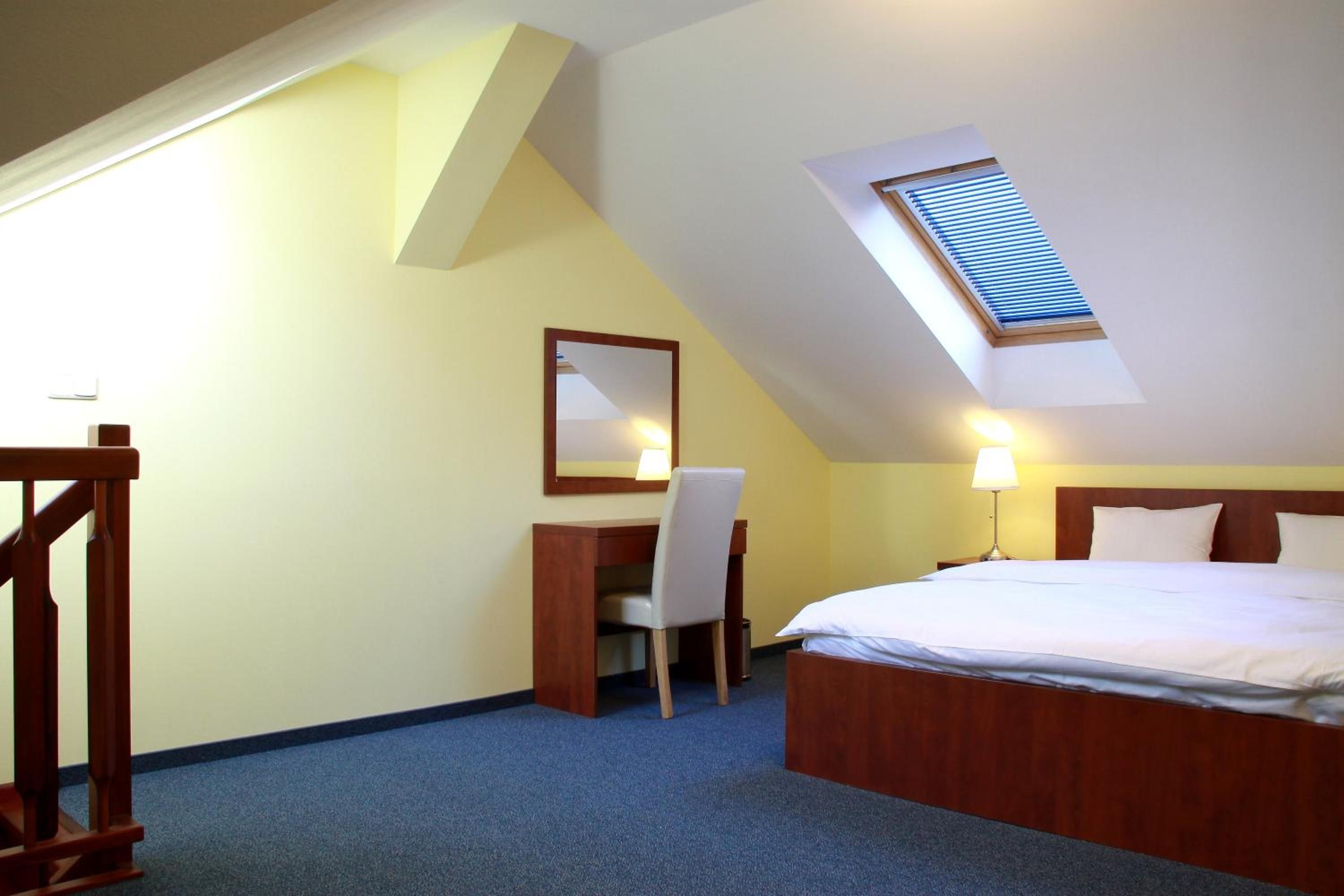 A hotel room with a bed, desk, chair, and a skylight.