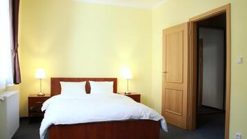 Ein Hotelzimmer mit einem Bett, zwei Nachttischen mit Lampen, einer Heizung und einer Tür zu einem anderen Raum.