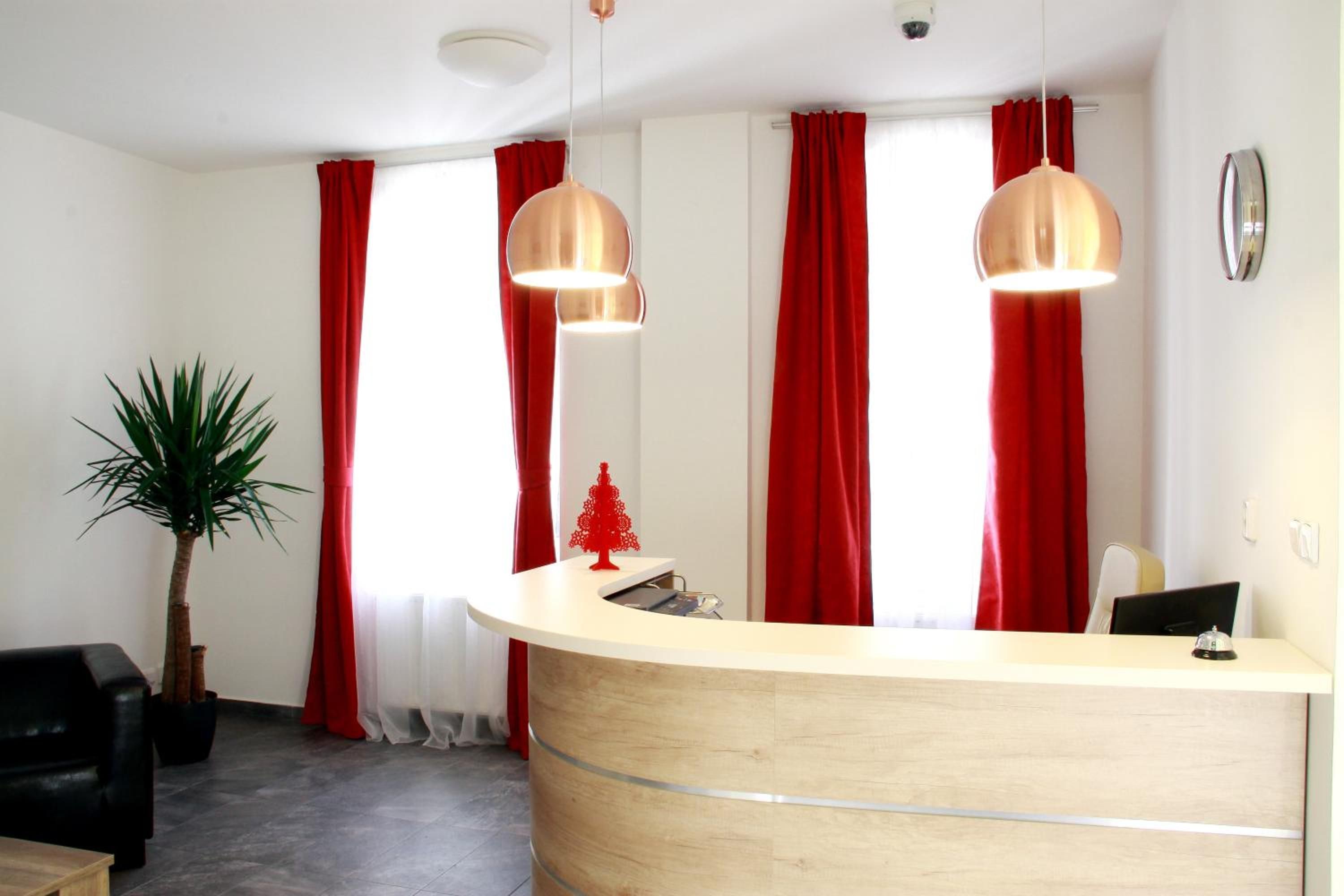A reception desk with a wooden finish, two pendant lights, red curtains, a small red Christmas tree, and a potted plant.