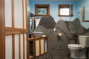 Casa de banho com design de parede de pedra, armários de madeira, pia e sanita.