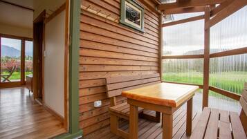 Interior de madeira com uma mesa e banco, um quadro na parede e vista para o verde lá fora.